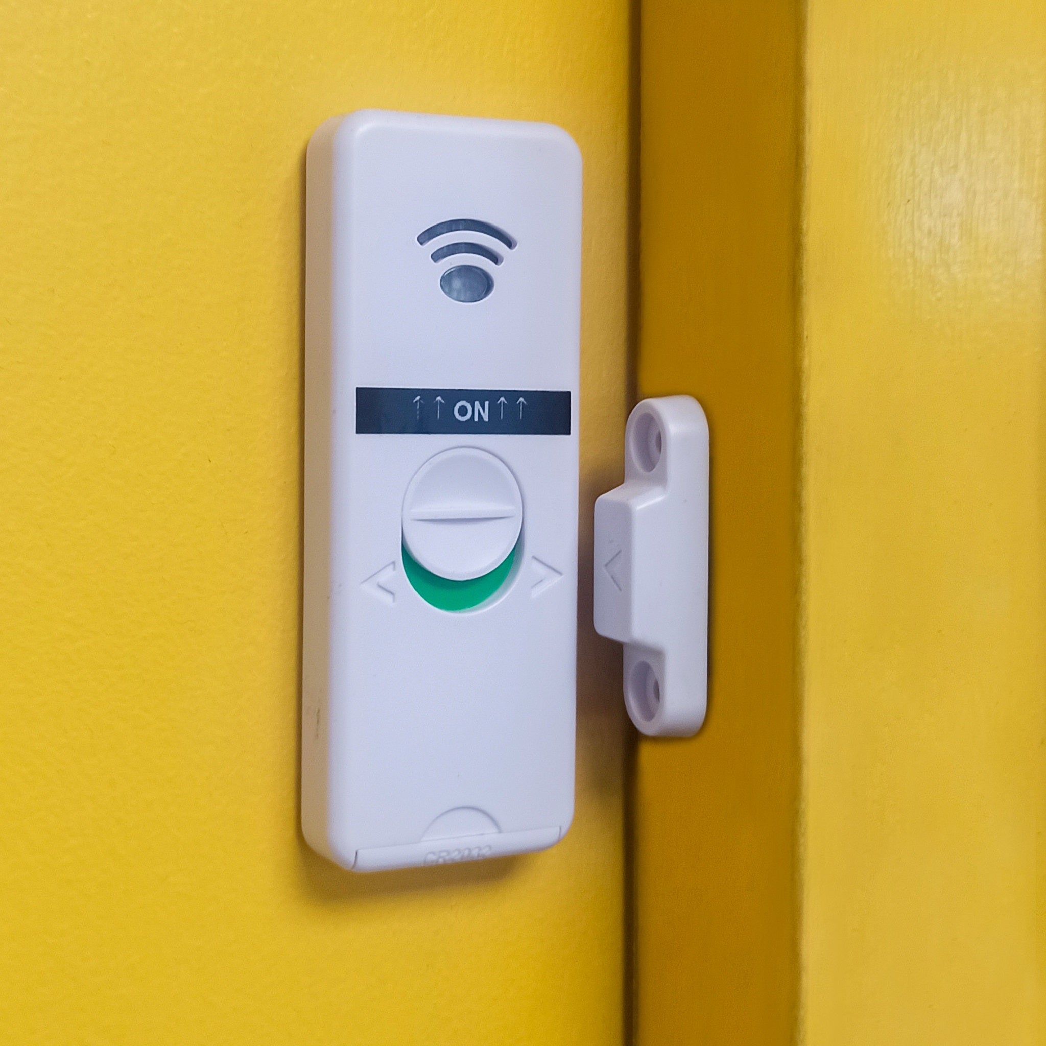Wall-mounted wireless door sensor activated against a yellow backdrop
